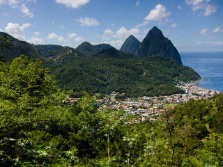 Fototapeta na wymiar The Two Pitons mountains named Gros Piton and Petit Piton on the coast of St Lucia with a blue ocean and the homes and houses of the island in foreground with forested hillsides