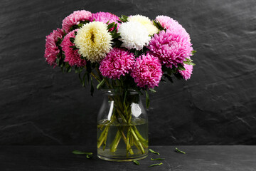 Beautiful asters in vase on table against black background. Autumn flowers