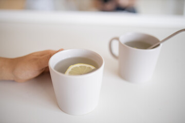 Hand holding a cup of lemon tea with a lemon slice inside