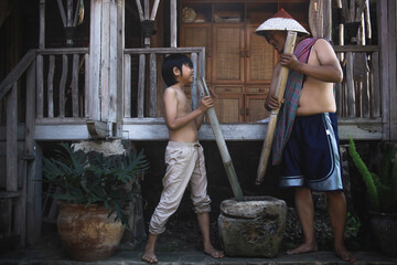 Two asian farmers looking at each other and pound using traditional mashing tools. Traditional...