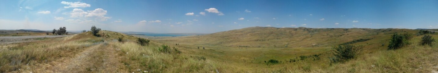 Fototapeta premium Steppes of Stavropol Territory Panorama Stavropol Territory. Summer sunny day. Blue sky with rare clouds. Steppe with grass burnt out in the sun. Green bushes. Endless spaces.