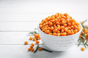 Fresh ripe sea buckthorn in bowl on white wooden table. Space for text