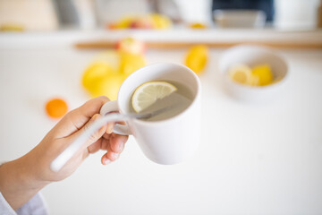 Hand holding a cup of lemon tea with a straw and lemon slice