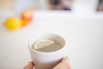 Hand holding a cup of lemon tea with a lemon slice inside