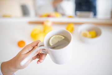 Hand holding a cup of lemon tea with a straw and lemon slice