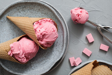 Obraz na płótnie Canvas Delicious pink ice cream in wafer cones with candies on grey table, flat lay