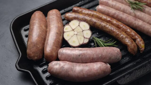 Sausages, sausages and tomatoes on a grill pan, dark background. The camera moves sideways. Close-up