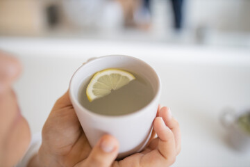 Woman gently blowing on a cup of lemon tea with a lemon slice inside