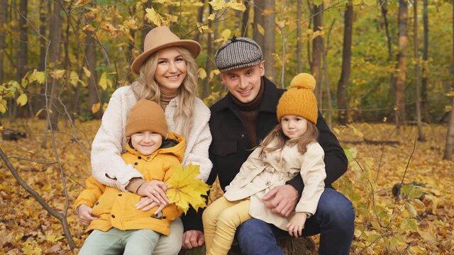 Positive family with children sit on stump in forest laughing, caucasian family have fun, smile, sit posing at camera. Autumn sunny day.