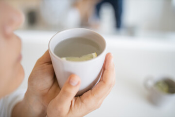 Woman gently blowing on a cup of lemon tea with a lemon slice inside