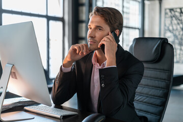 Young businessman wearing black suit, sitting to table with computer making a call. Office manager...