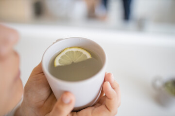 Woman gently blowing on a cup of lemon tea with a lemon slice inside