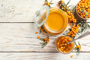 Delicious sea buckthorn jam and fresh berries on white wooden table, flat lay. Space for text