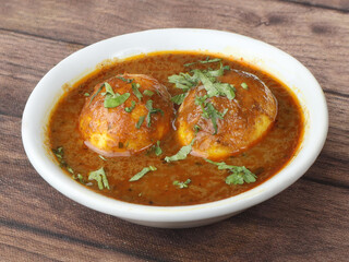 Anda Masala or Egg Curry is popular indian spicy food, served in a ceramic bowl over rustic wooden background. Selective focus