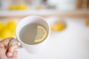 Hand holding a cup of lemon tea with a lemon slice inside