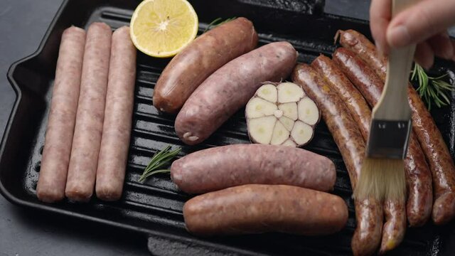 A girl greases grilled sausages with butter on a grill pan with lemon, rosemary and garlic. Close-up. The camera moves sideways