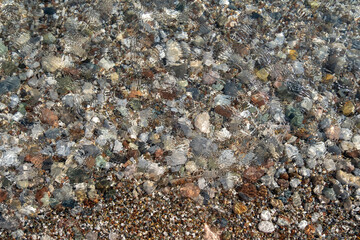 Large and small multi-colored pebble stones on the beach under clear water with ripples