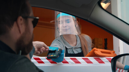 Bearded man driver in car paying with credit card for fast food order at drive thru counter