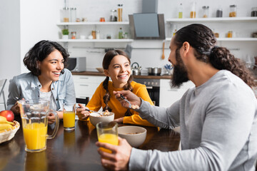Cheerful hispanic family looking at each other during breakfast with cereals and orange juice in kitchen