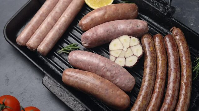 Sausages, sausages and tomatoes on a grill pan, dark background, the camera moves forward. Close-up