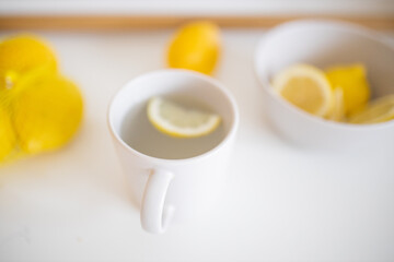 Cup of lemon tea on a white table surrounded by lemons
