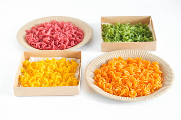Multicolored pasta in a disposable kraft paper plates and boxes on a white background. Copy, empty space for text
