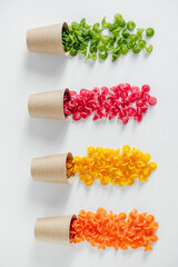 Multicolored pasta in a disposable kraft paper cups scattered on a white background. Top view. Copy, empty space for text