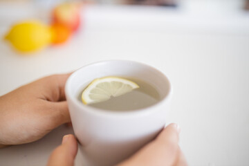 Hands holding a cup of lemon tea with a lemon slice inside
