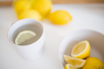 Cup of lemon tea on a white table surrounded by lemons