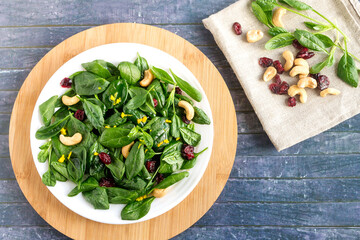 Fresh vitamin salad of spinach leaves, nuts, dried cranberries on a kitchen board in a white plate.