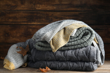 Stack of knitted plaids with dry leaves on wooden table, closeup