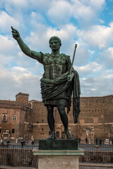 Bronze statue of the Roman Emperor Augustus on Via dei Fori Imperiali in front of old brick buildings near the Roman Forum, Rome, Italy.