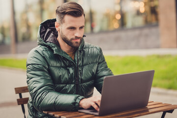 Photo of charming cute young guy dressed green coat having rest sitting cafeteria writing modern gadget outdoors city street © deagreez
