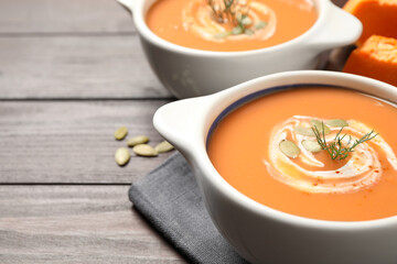 Tasty creamy pumpkin soup with dill and seeds in bowl on wooden table. Space for text