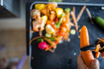 Female hands peeling a carrot on top of organic trash