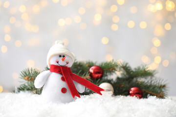 Fototapeta na wymiar Snowman toy on snow against blurred festive lights, space for text. Christmas decoration