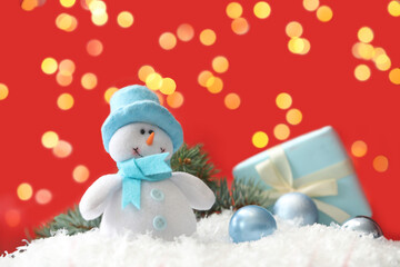 Snowman toy and Christmas balls on snow against blurred festive lights