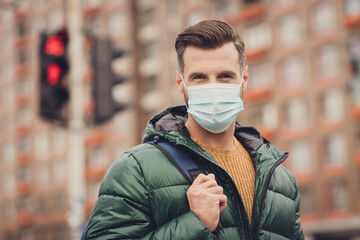 Photo of serious confident handsome young man wear green windbreaker schoolbag face respirator...