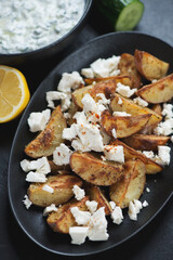 Baked potato wedges served with feta cheese and tzatziki in a greek style, vertical shot, close-up