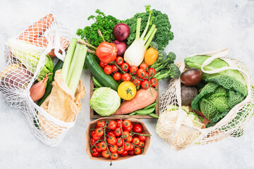 Zero waste shopping concept. Variety of organic vegetables in brown box, reusable bags. Healthy raw produce on white wooden table, top view, selective focus