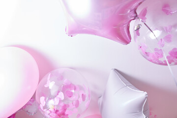 Pink, white and transparent balloons with rose petals inflated with helium on a white background