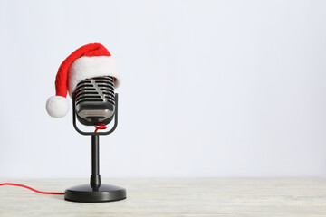 Retro microphone with Santa hat on wooden table against white background, space for text. Christmas...