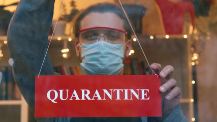 Young male seller in protective mask hanging quarantine sign on entrance door