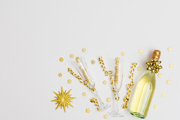 Festive white background with gold decoration , bottle of sparkling wine with two crystal glasses, shiny golden serpentine confetti and glittering snowflakes, golden star, copy space, top view