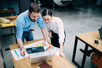 Young coworkers using laptop and documents at office