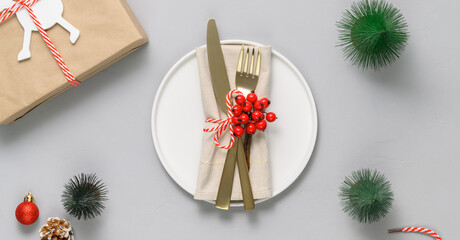 Festive table setting with white plate, golden cutlery and xmas decorations on light gray tabletop....