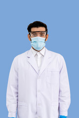 Portrait of confident male Middle Eastern Arab researcher scientist medical doctor wearing surgical mask and protection glasses standing  isolated on light blue background