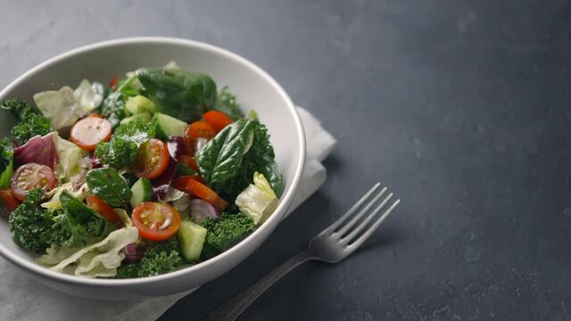 The camera moves along a salad of juicy fresh farm vegetables - cucumbers, tomatoes, lettuce leaves. Dark background, place for text, close-up. 4K