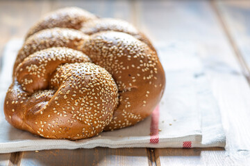 Traditional Jewish sweet Challah bread for Shabbat on a white textile on a wooden table, close up.