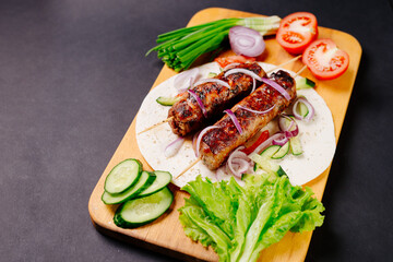 Grilled lula kebab on pita bread with vegetables on a dark background
